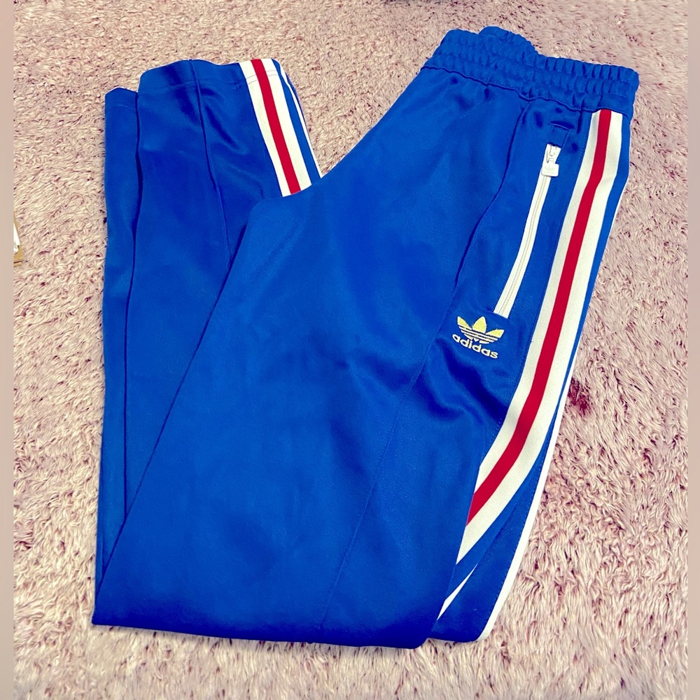 Blue Men’s track pants with red and white stripes and zippered pockets .